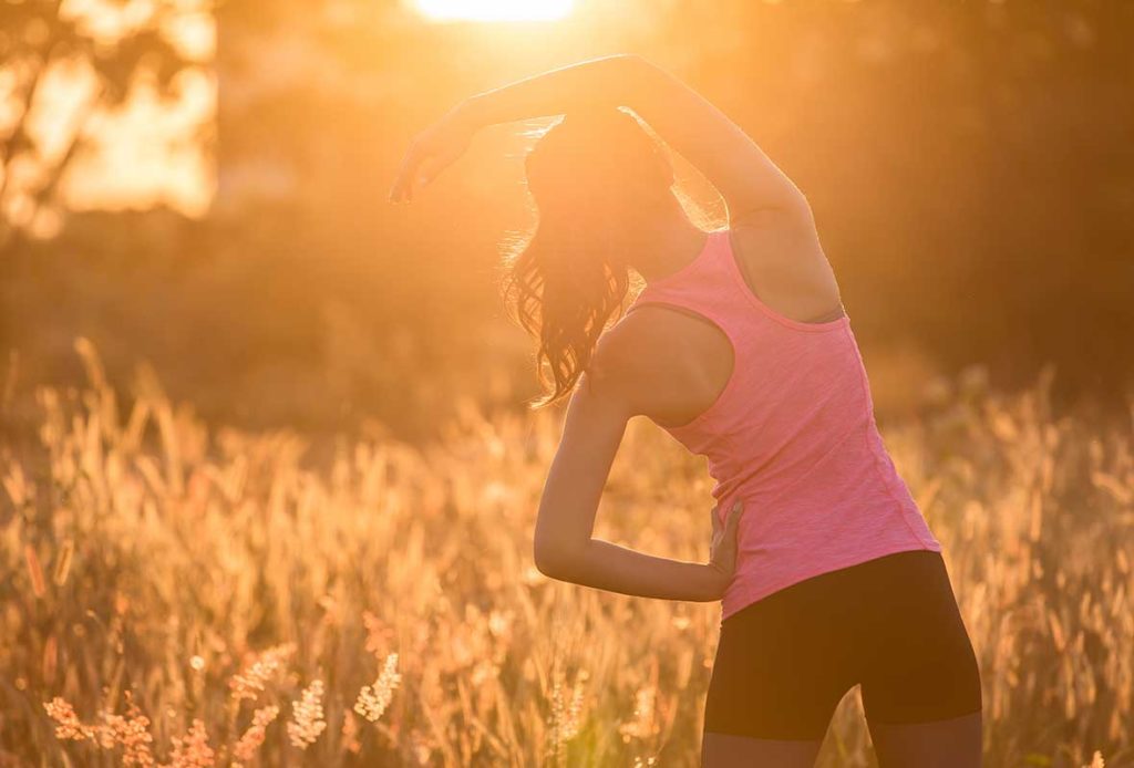 A woman in yoga gear stretching outside at sunset