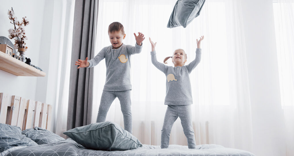 Two children jumping on a bed and playing with pillows