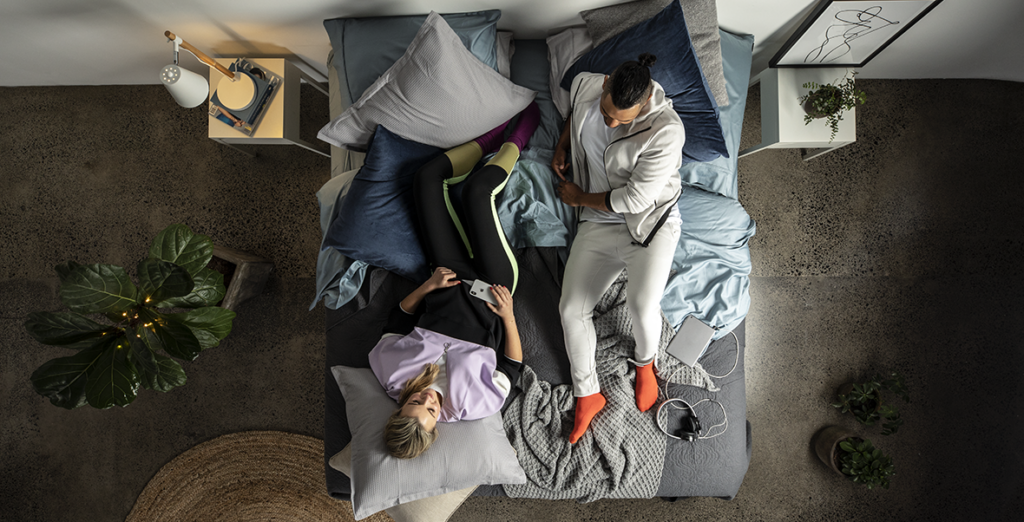 A happy couple lying on either end of a SleepMaker mattress in a casual bedroom