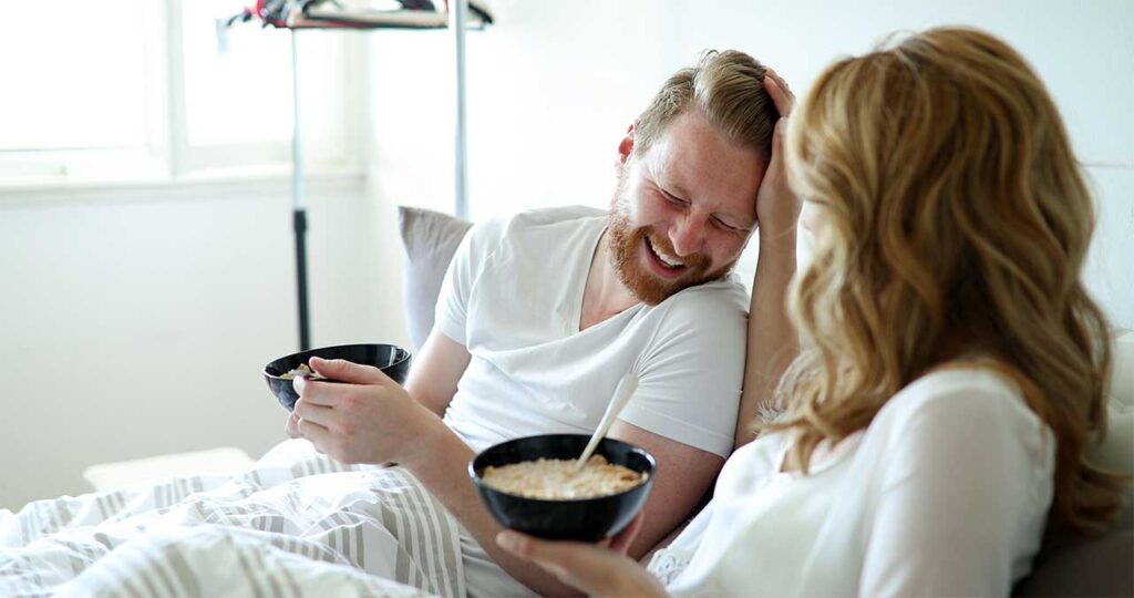 A man and a woman eating cereal in bed