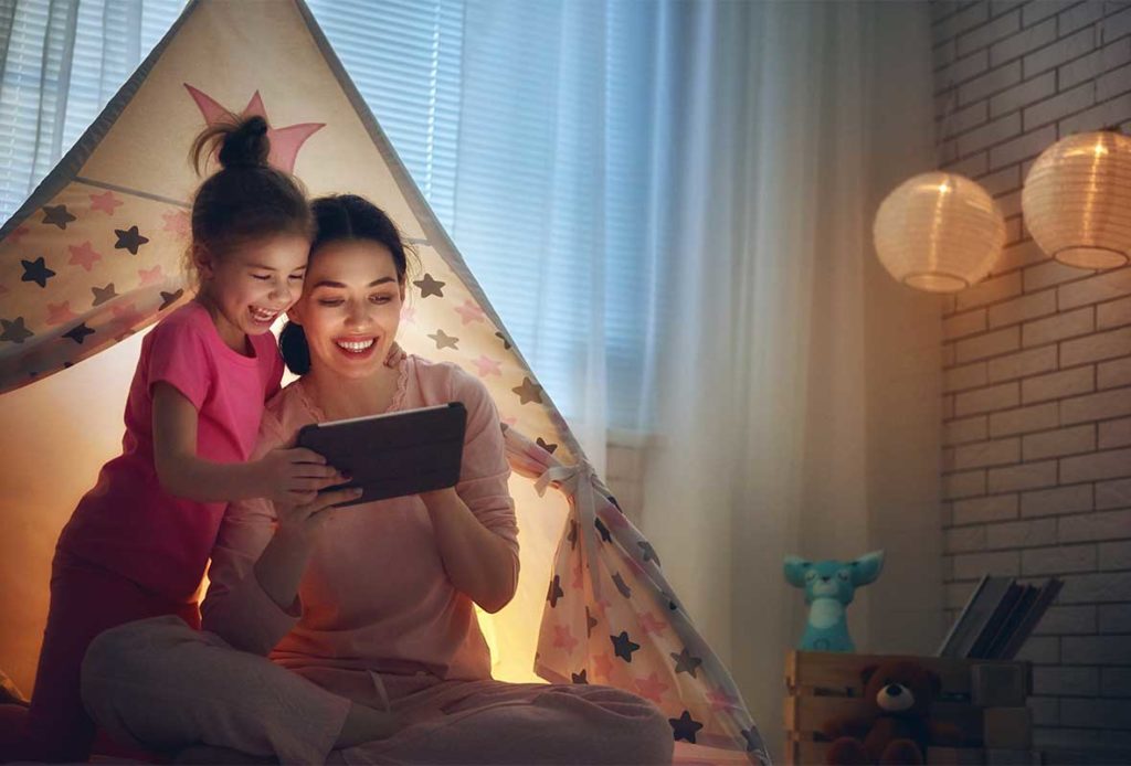 A mother and daughter inside an indoor tent, smiling and looking at a tablet screen