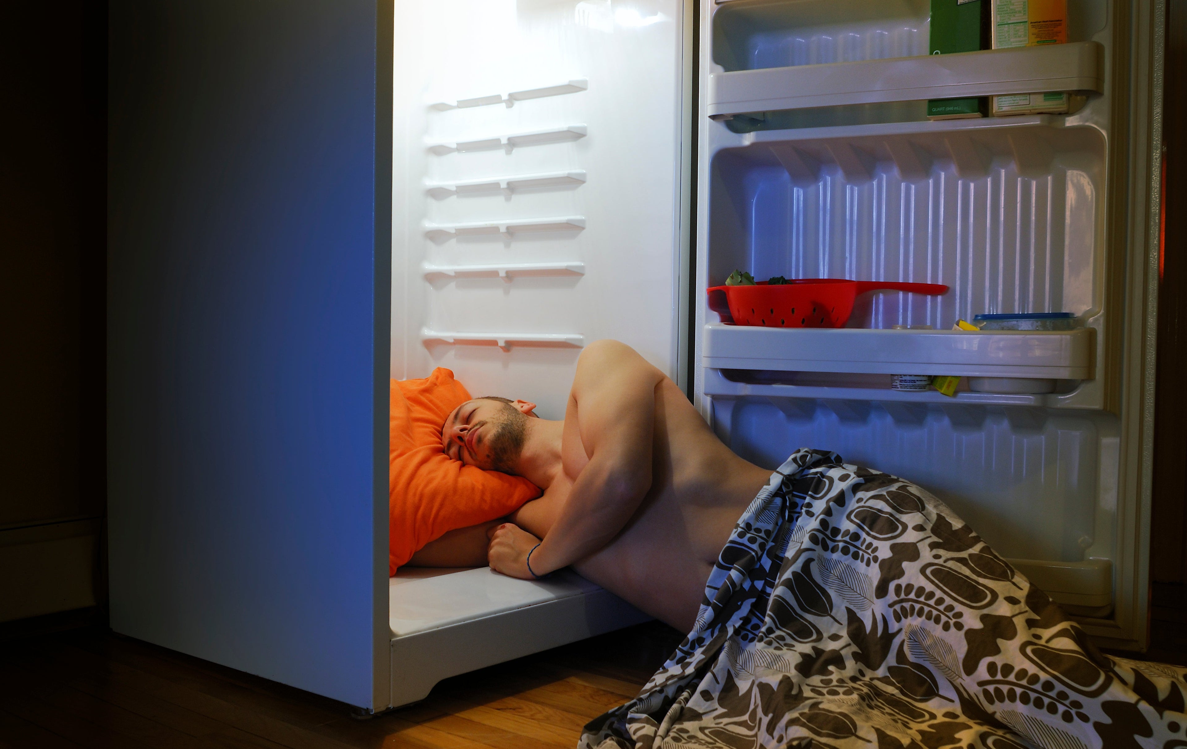 A man sleeping with his head on a pillow inside the fridge