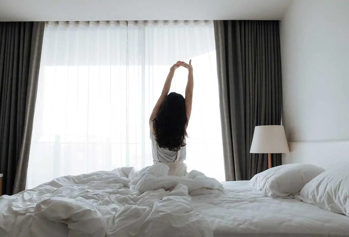 A woman sitting on her bed stretching in front of a window