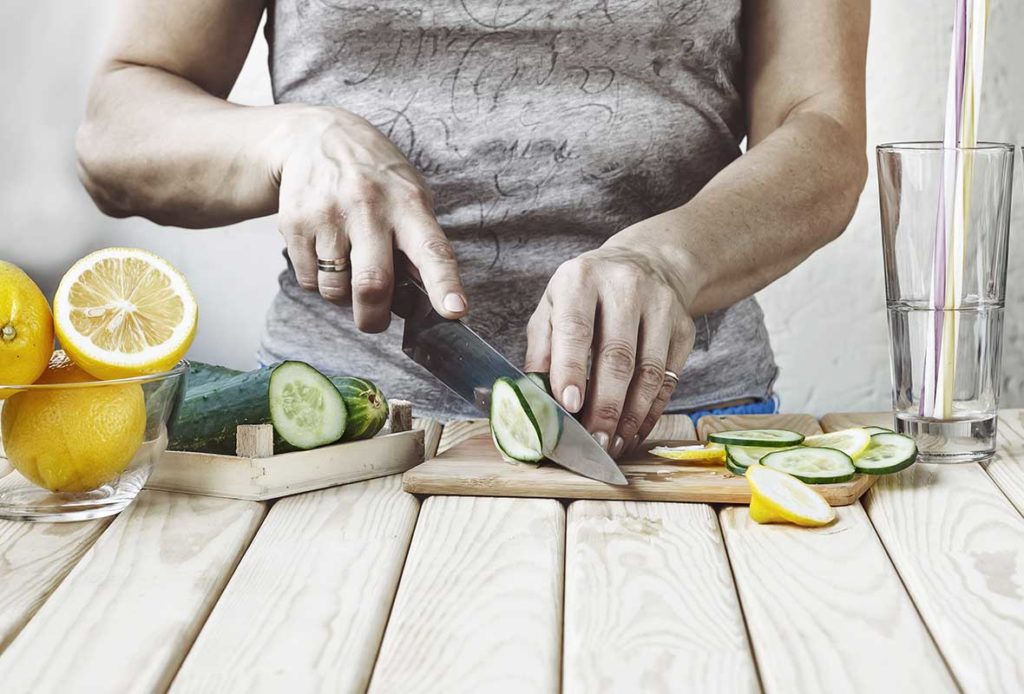 A woman cutting up lemons in cucumber on a wooden cutting board