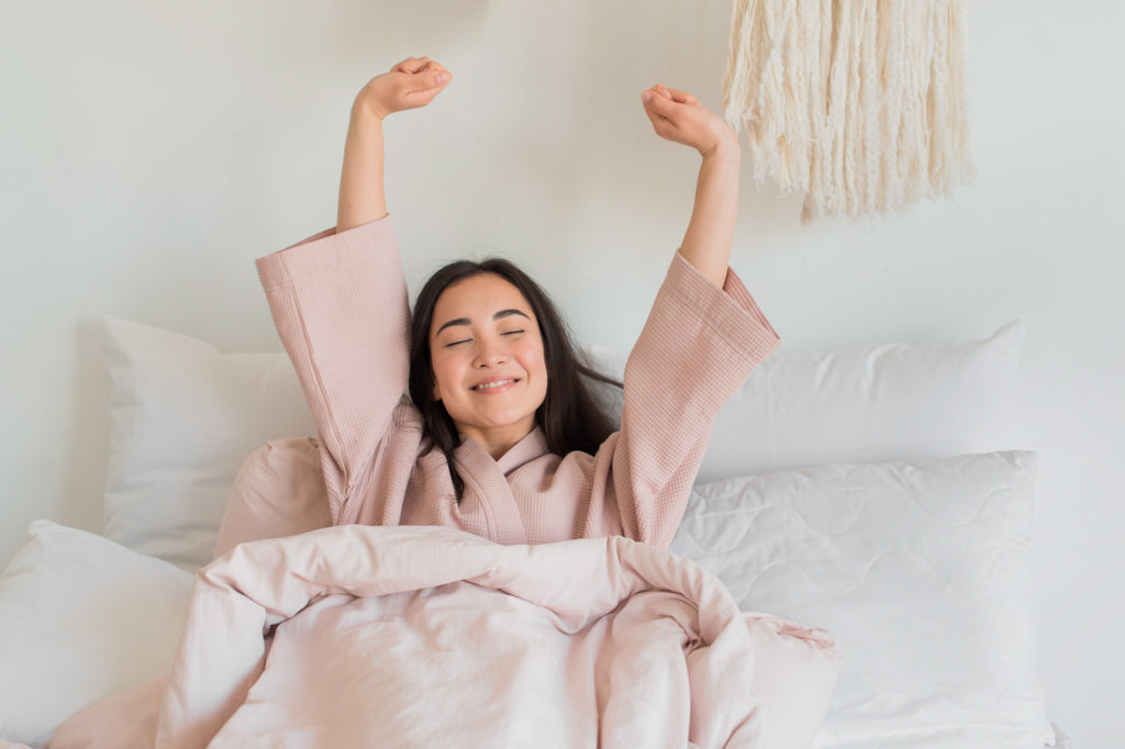 A happy woman sitting up in bed stretching her arms over her head