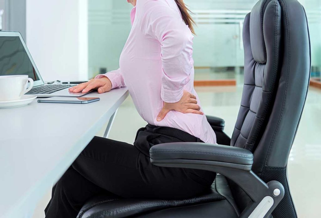 A woman sitting on an office chair, holding her lower back