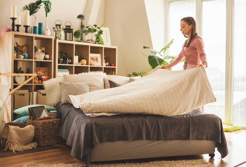 A woman changing the bedding on her bed
