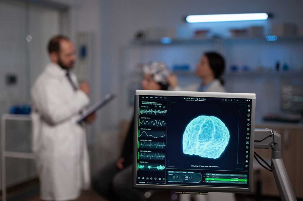 A monitor displaying a 3D scan of a brain, health workers in the background.