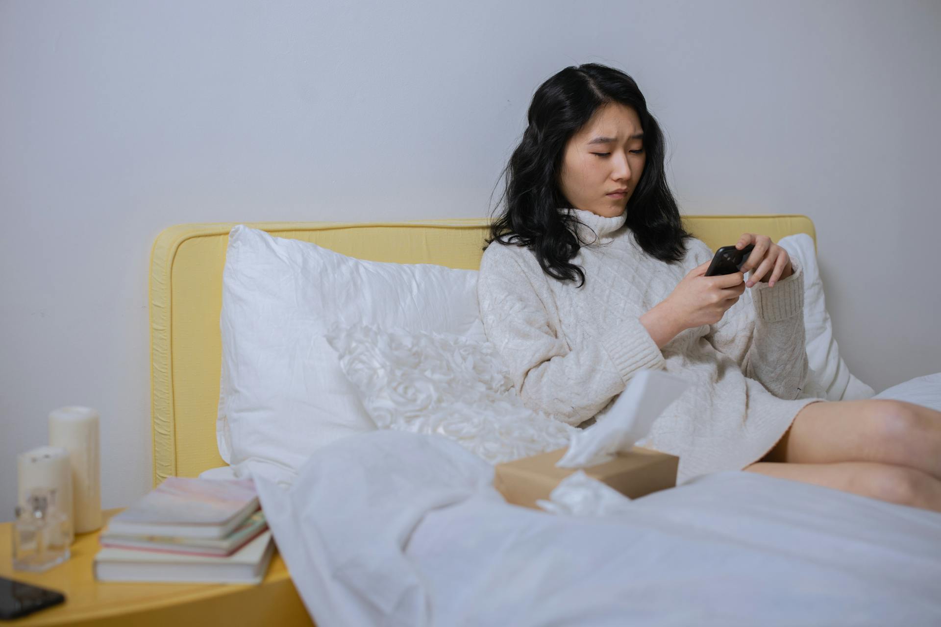 A young woman sitting in bed using her phone