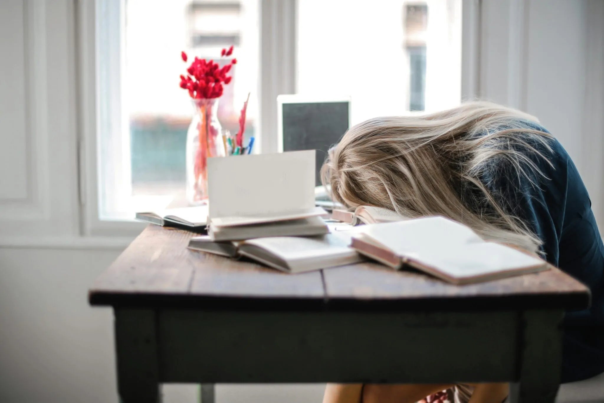 A woman sleeping in the middle of the day, her head resting on a desk covered in books