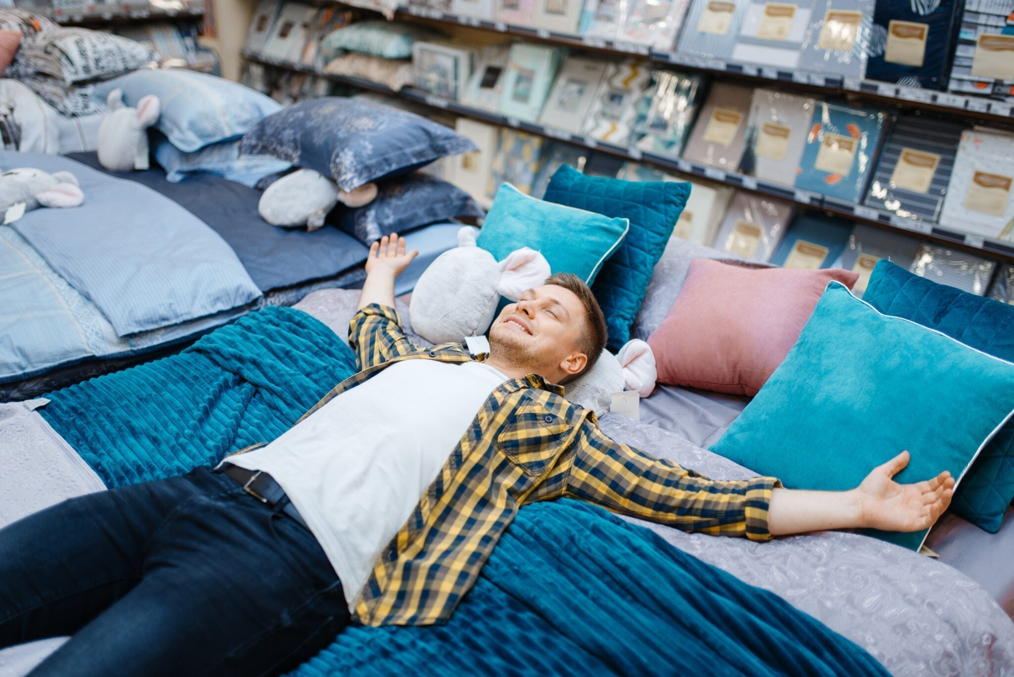A man smiling and lying on a bed in a furniture store