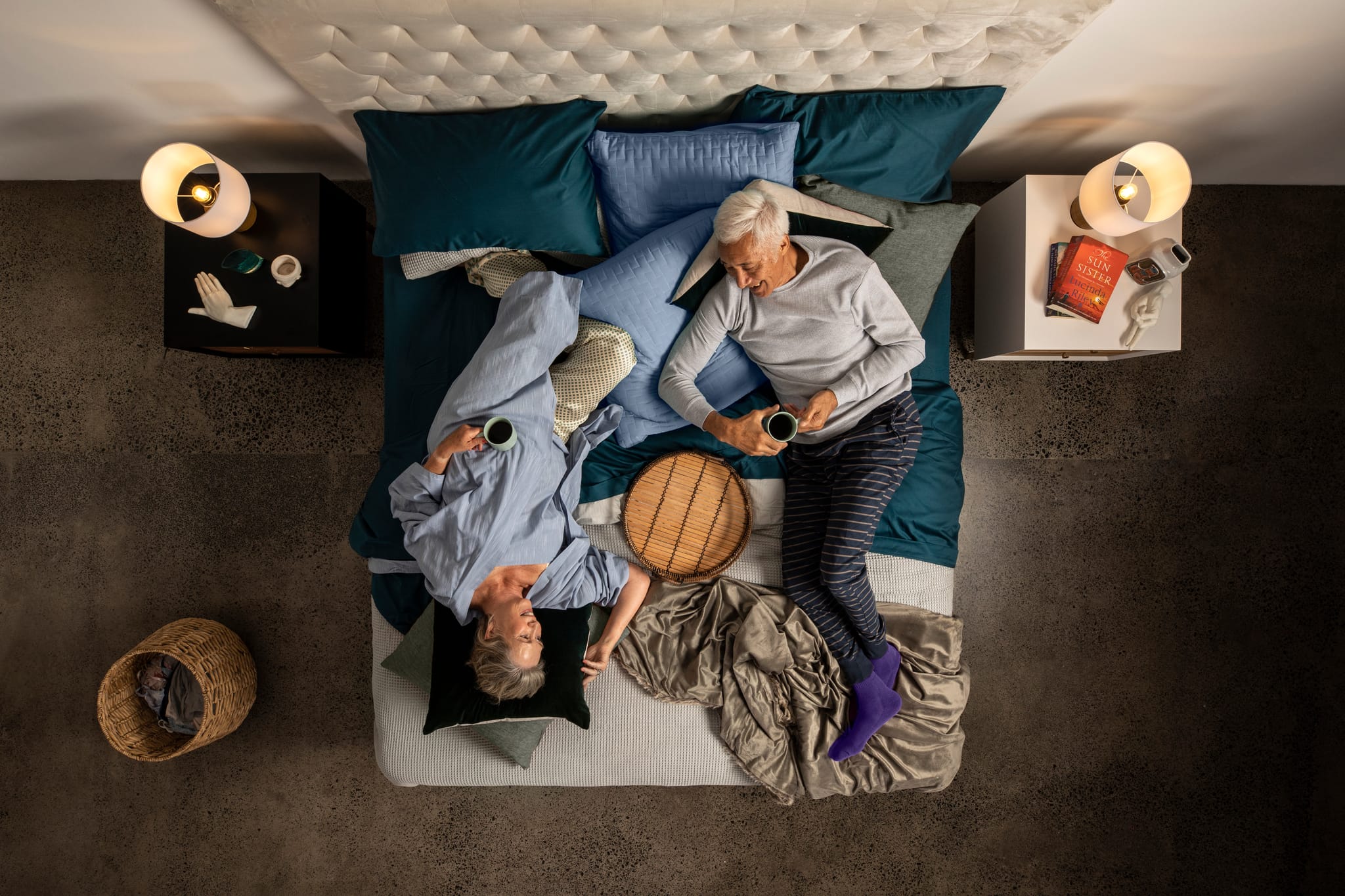 Two people reclining on a SleepMaker bed in a cozy room with candles and pillows.