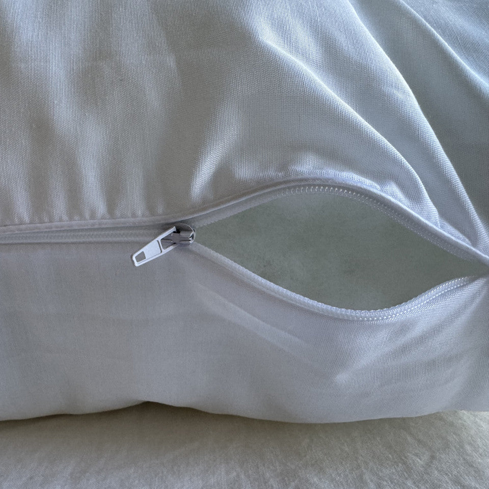 Close-up of a white pillow cover with a zipper opening, showing the smooth material and silver zipper pull.