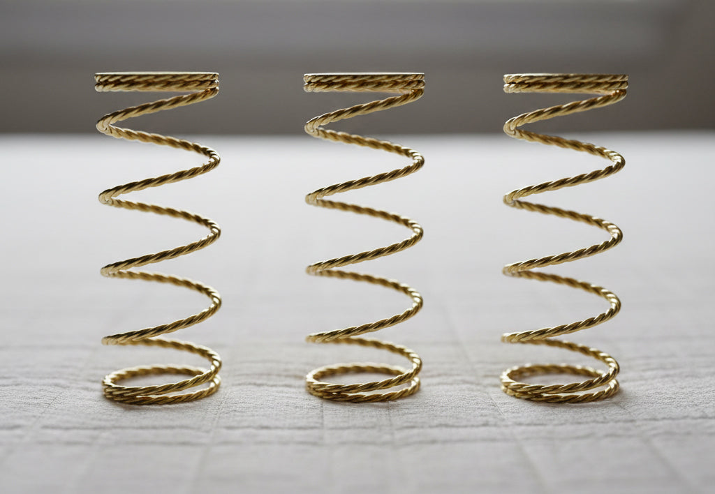 Three gold-colored twisted metal coil Q4 springs standing vertically on a light gray textured surface.