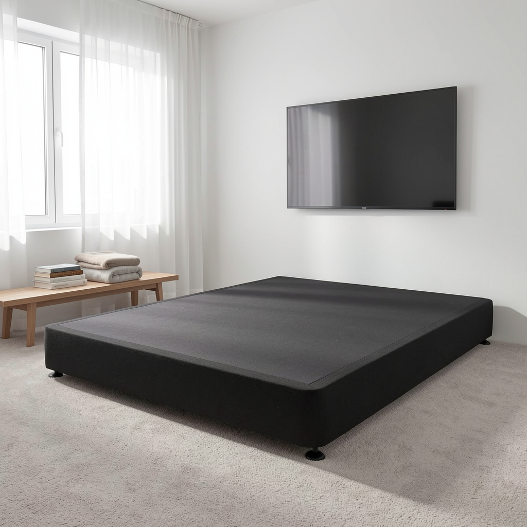 A black upholstered bed frame with a mattress, shown in a bright, modern bedroom with a wall-mounted TV, a small wooden bench, and sheer white curtains.