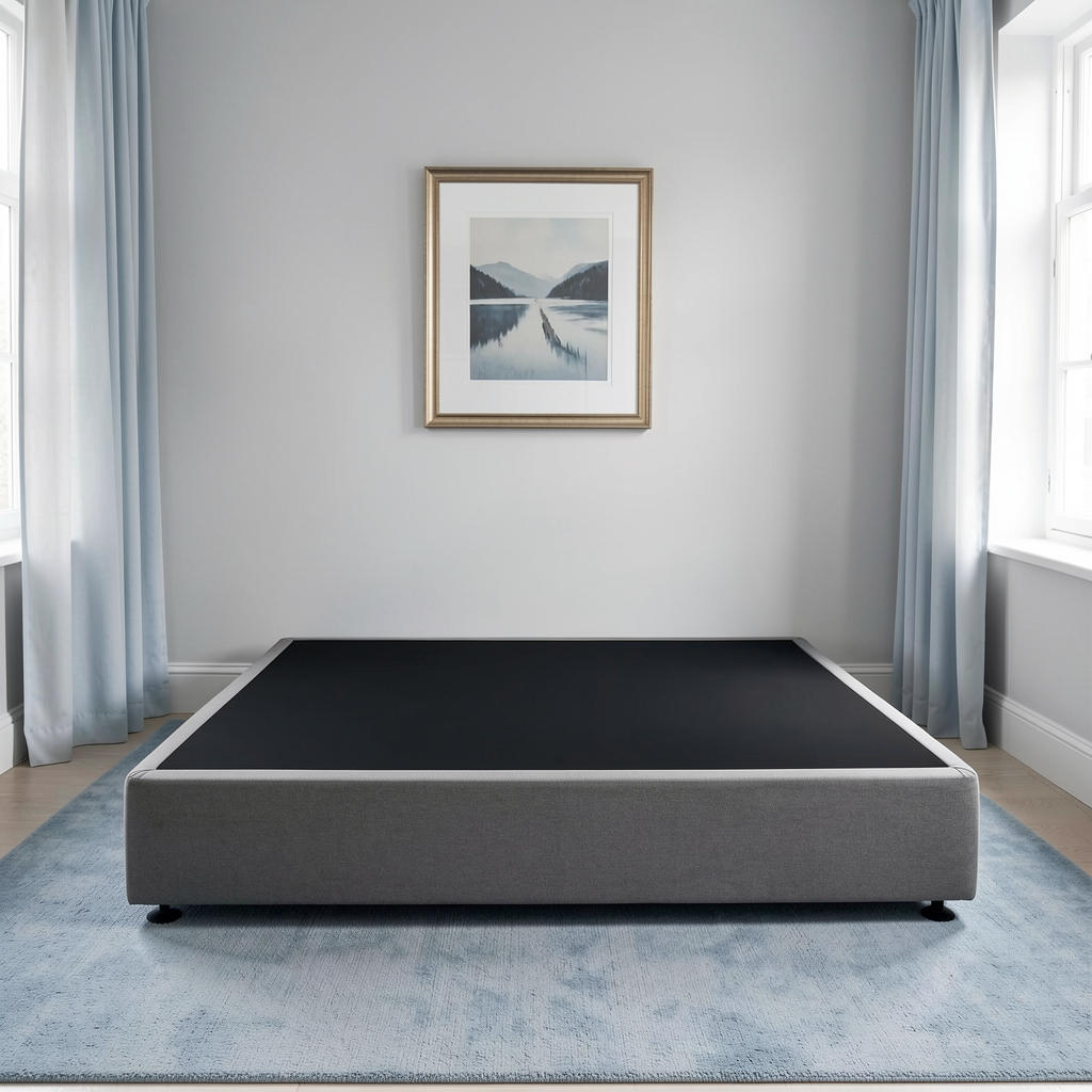 A low-profile platform bed base, set in a modern bedroom with a blue-gray rug, light gray walls, and blue curtains.